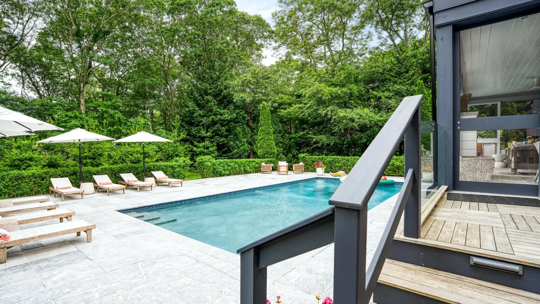An outdoor swimming pool is bordered by lounge chairs and surrounded by trees.
