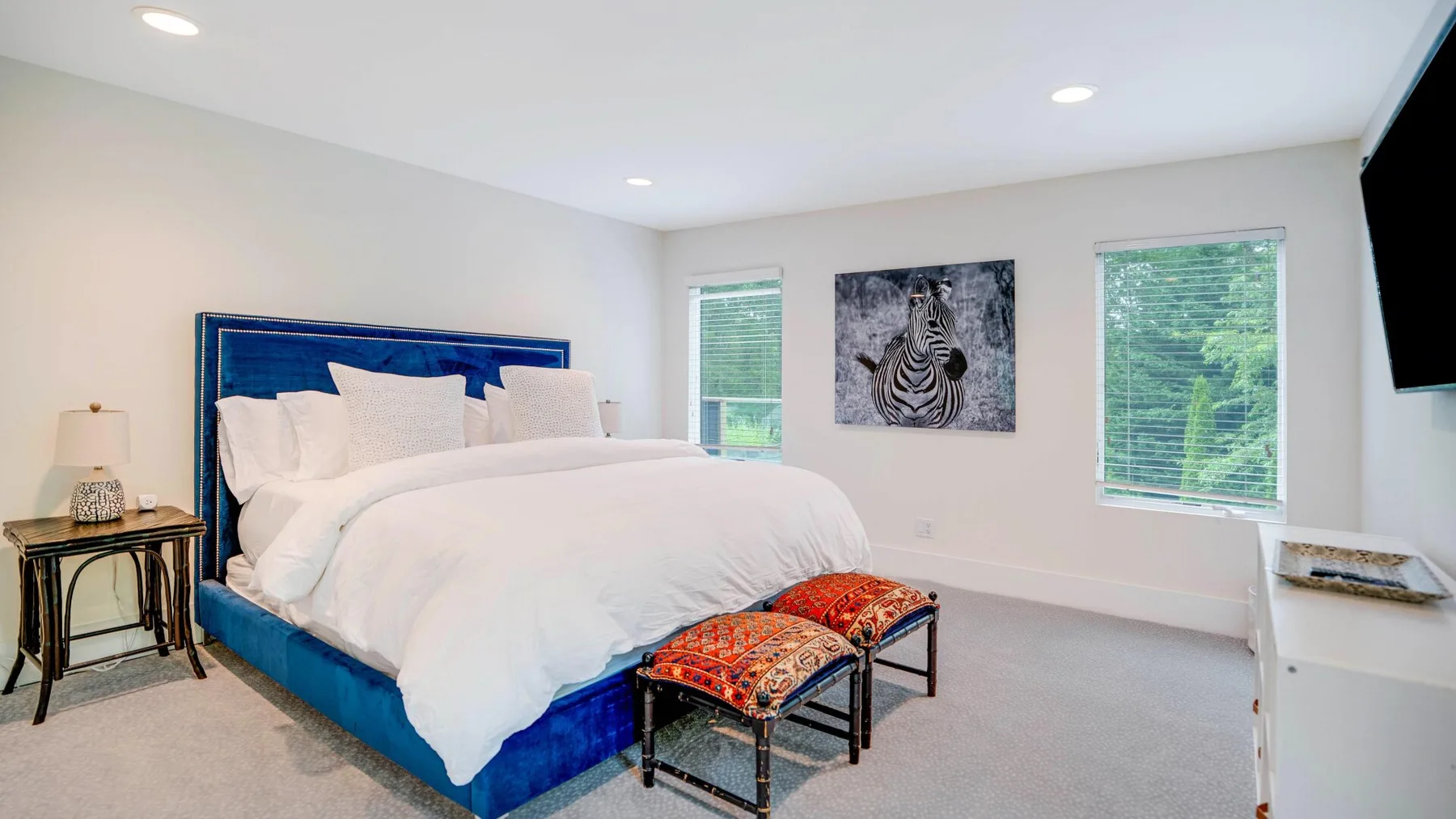 A bedroom with a bed, two window views, and zebra artwork on the wall.