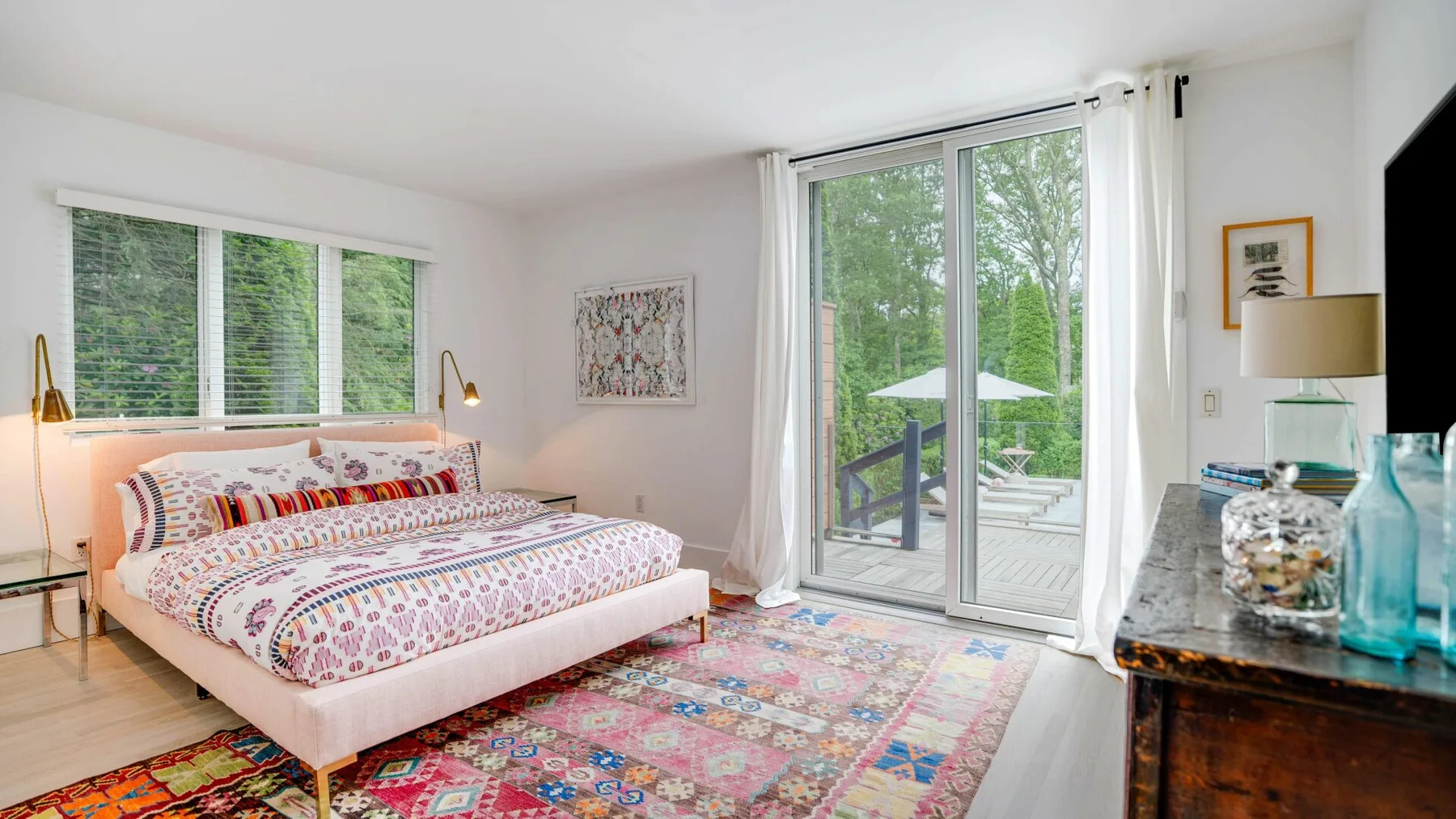 A bright bedroom with a patterned bed and sliding glass doors opening to greenery.