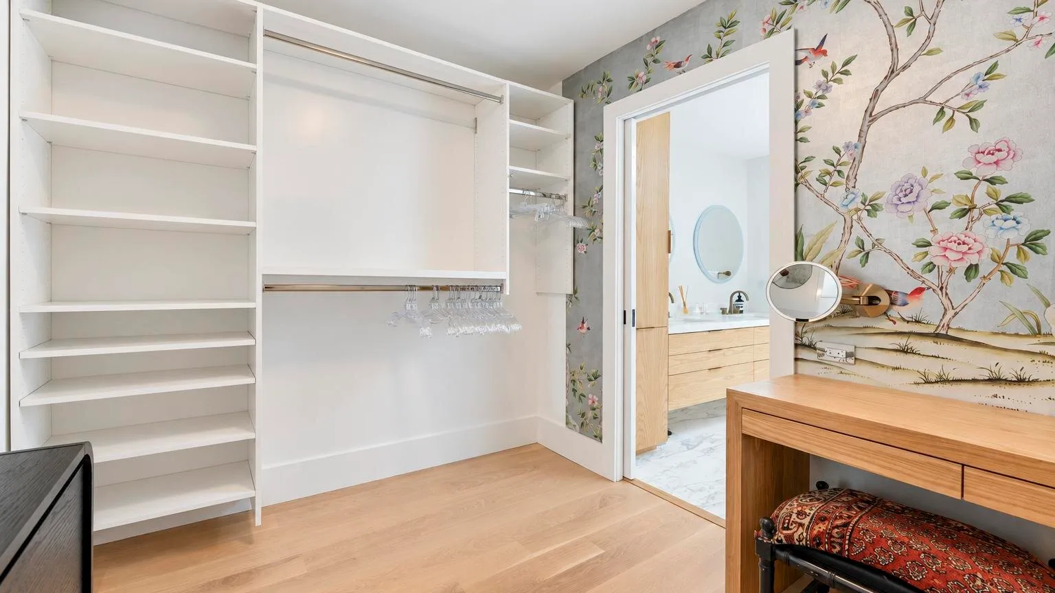 A bright dressing area with built-in shelving and an open doorway to a vanity.