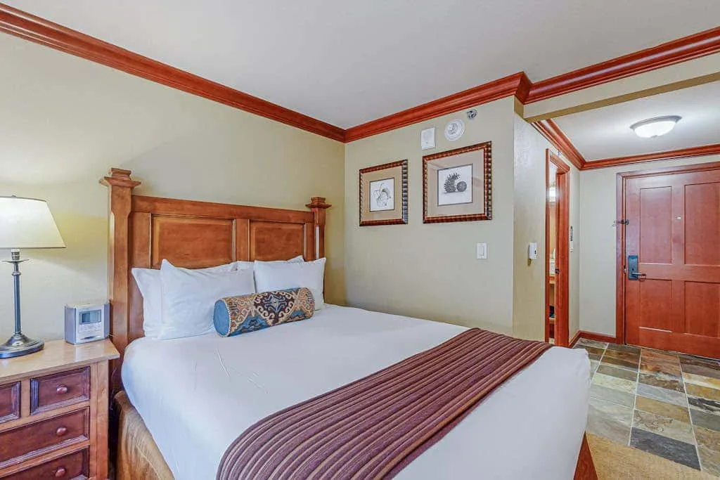 Un dormitorio con una cama de madera, ropa de cama blanca y una colcha a rayas.