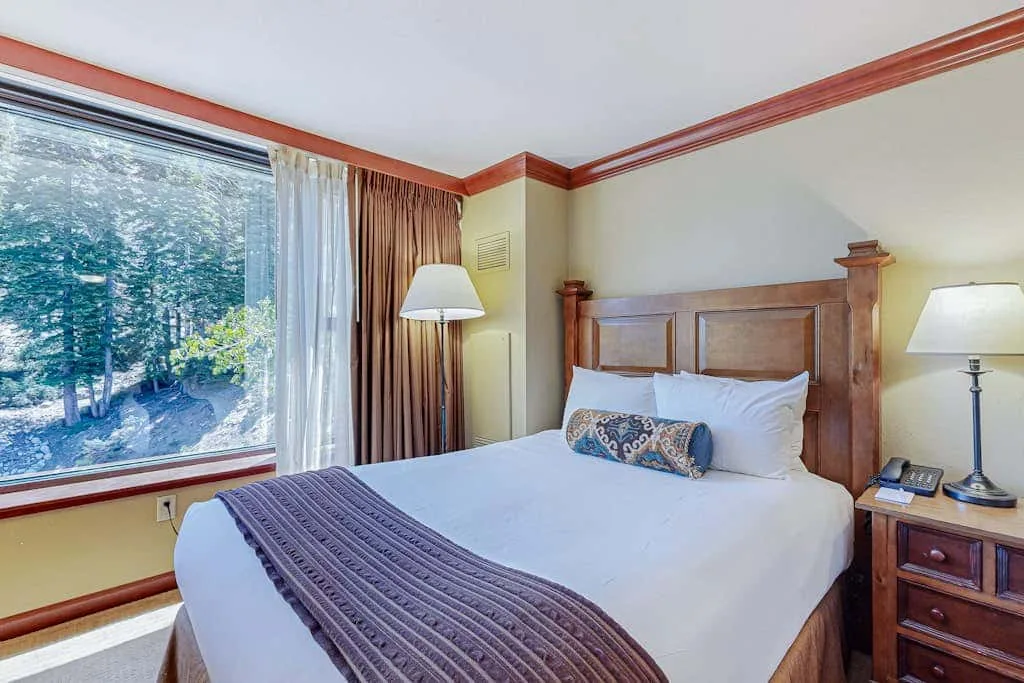 Un dormitorio con una cama bien tendida junto a una ventana grande.