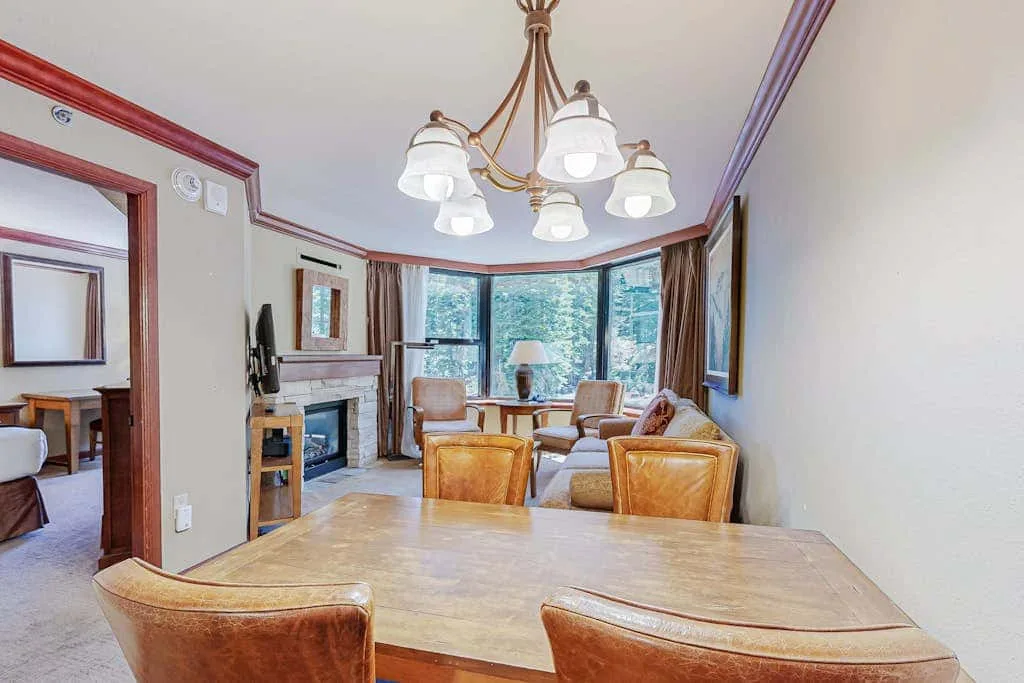 Una mesa de comedor y asientos dan a una sala de estar con grandes ventanas.