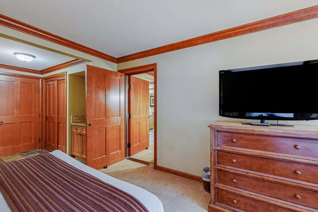 Un dormitorio con puertas de madera, un televisor y una cómoda junto a la cama.