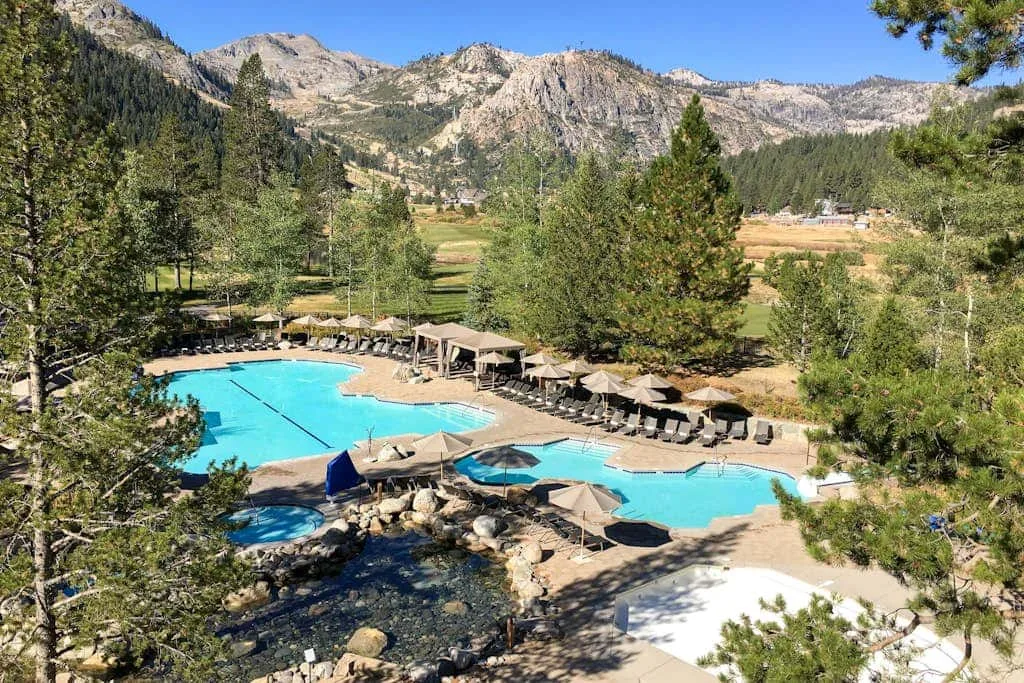 An outdoor swimming pool sits among trees, with mountain ridges in the background.