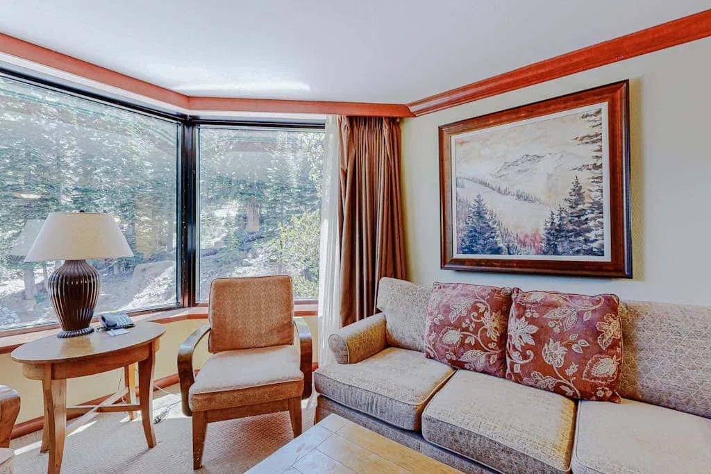 Living room seating beside corner windows, with a framed landscape painting above the couch.