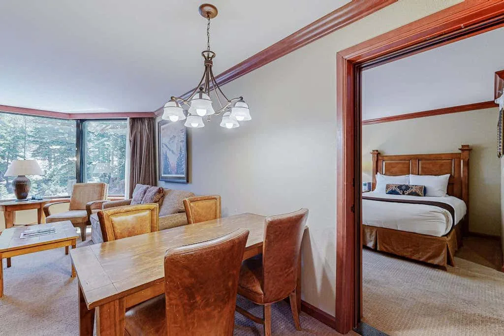 Un comedor con una mesa de madera y asientos junto a una sala de estar.