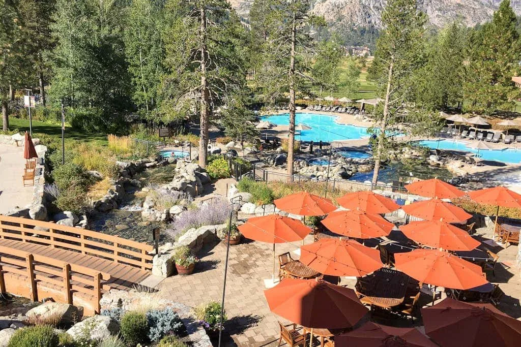Zona de piscina al aire libre con sombrillas naranjas y un arroyo rocoso ajardinado.
