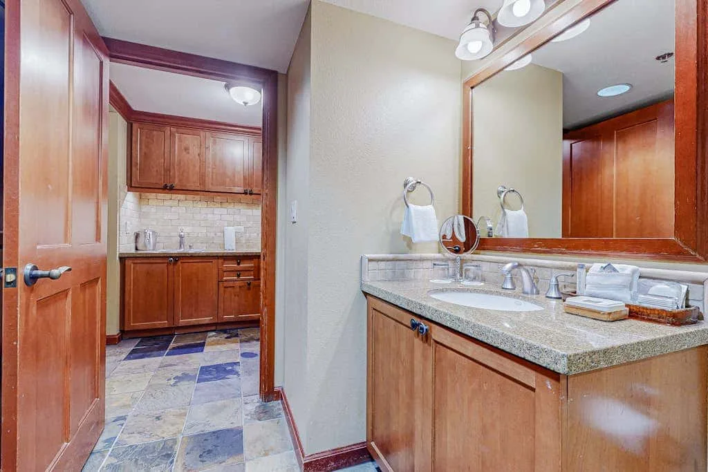 Un lavabo de baño con un espejo grande da a un suelo de baldosas y armarios de madera.