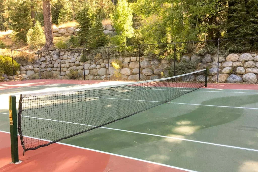 Una cancha de tenis al aire libre con una red y un muro de contención de piedra.
