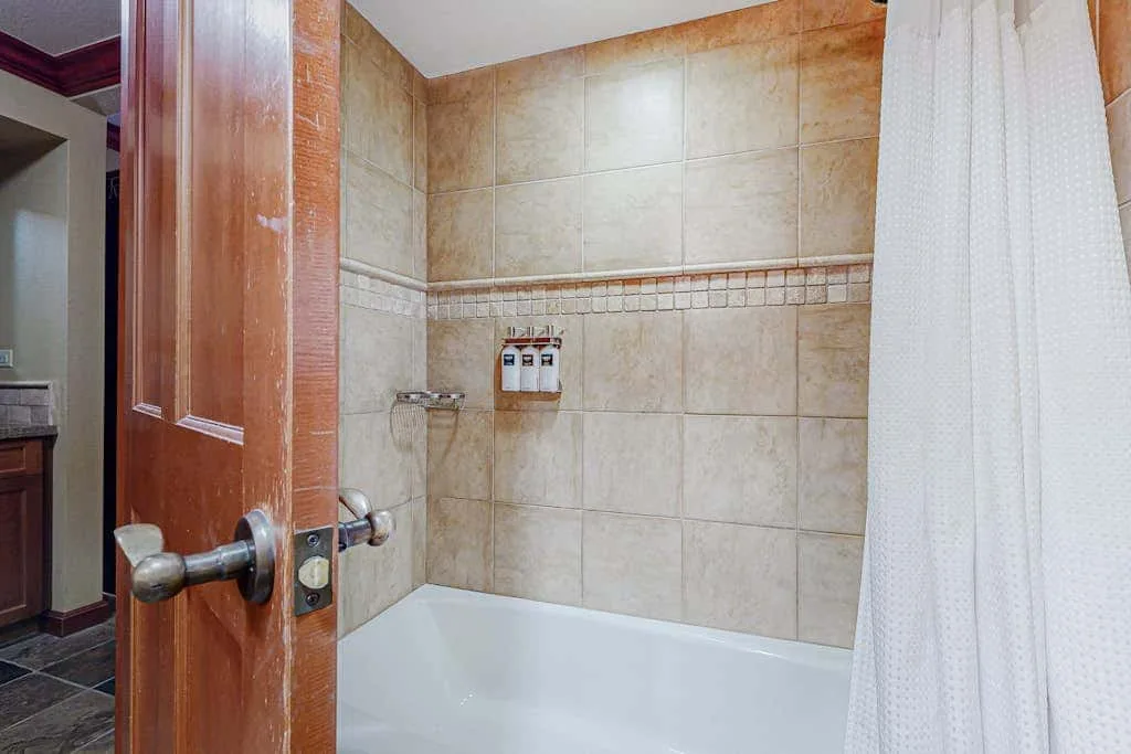 Un baño alicatado con bañera, grifería de ducha y una cortina blanca.