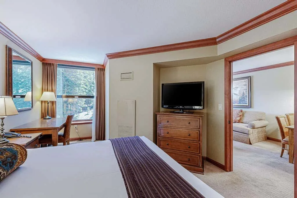 Un dormitorio con cama, escritorio y televisor junto a una entrada a una zona de estar.