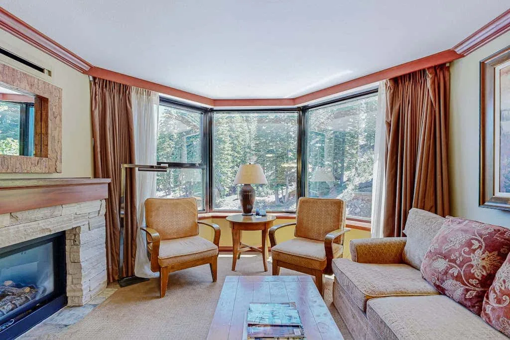 A bright living room with seating arranged around a coffee table beside large windows.