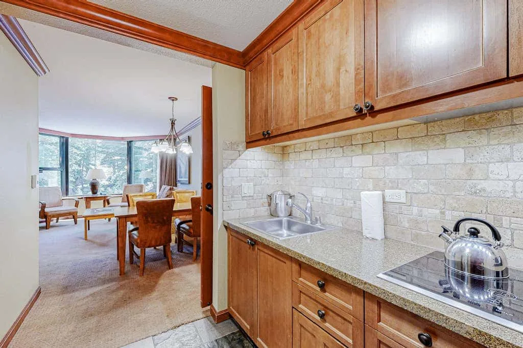 Una cocina con gabinetes de madera y una encimera se abre a un comedor y una sala de estar.
