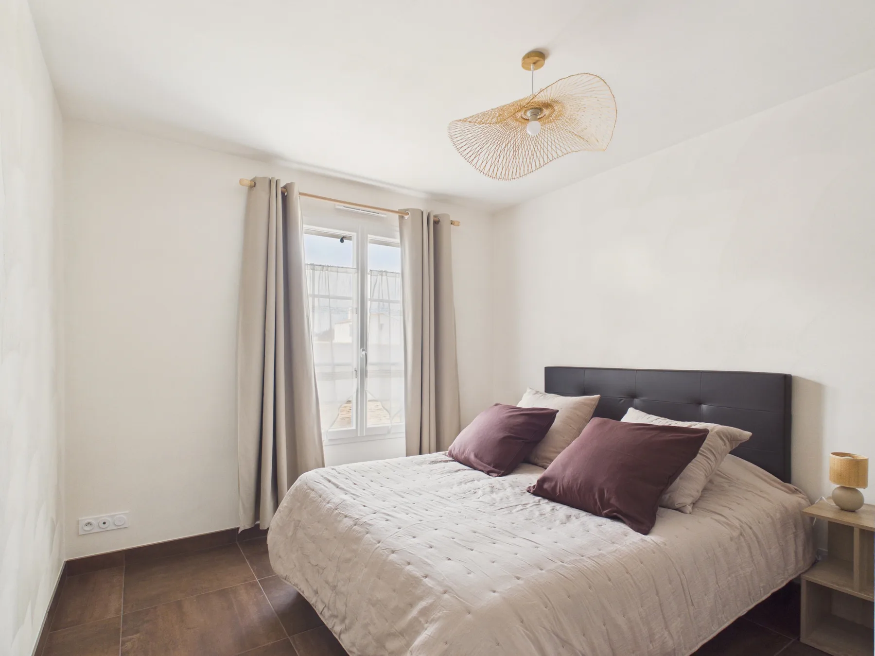 A bright bedroom with a large bed beside a curtained window.