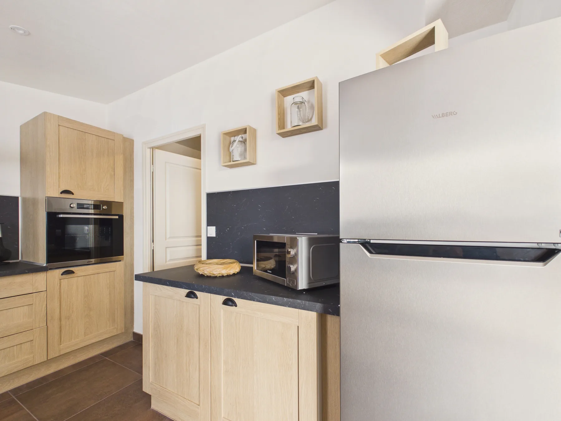 A modern kitchen with light wood cabinets, a refrigerator, and countertop appliances.