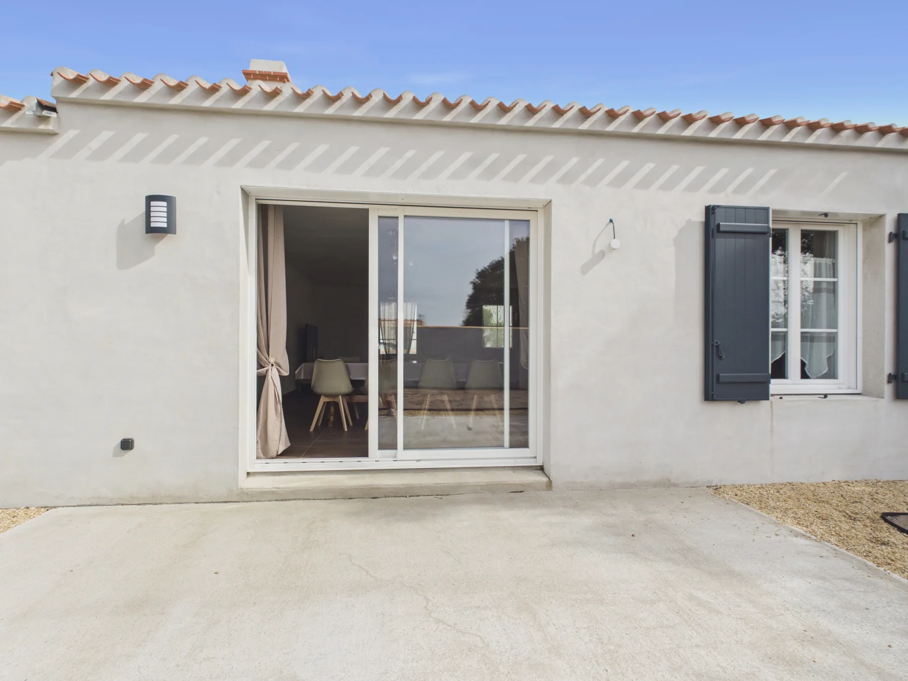 A white exterior wall with a sliding glass door opening onto a paved patio.