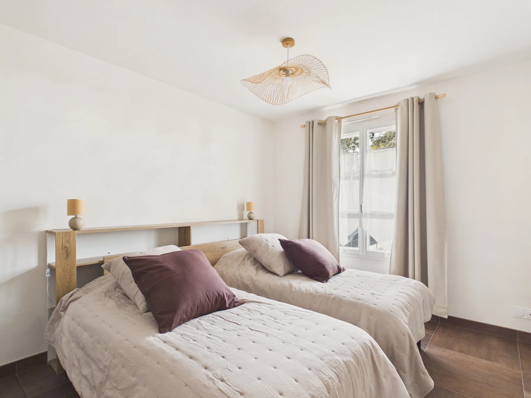 A bright bedroom with two beds and a window with curtains.