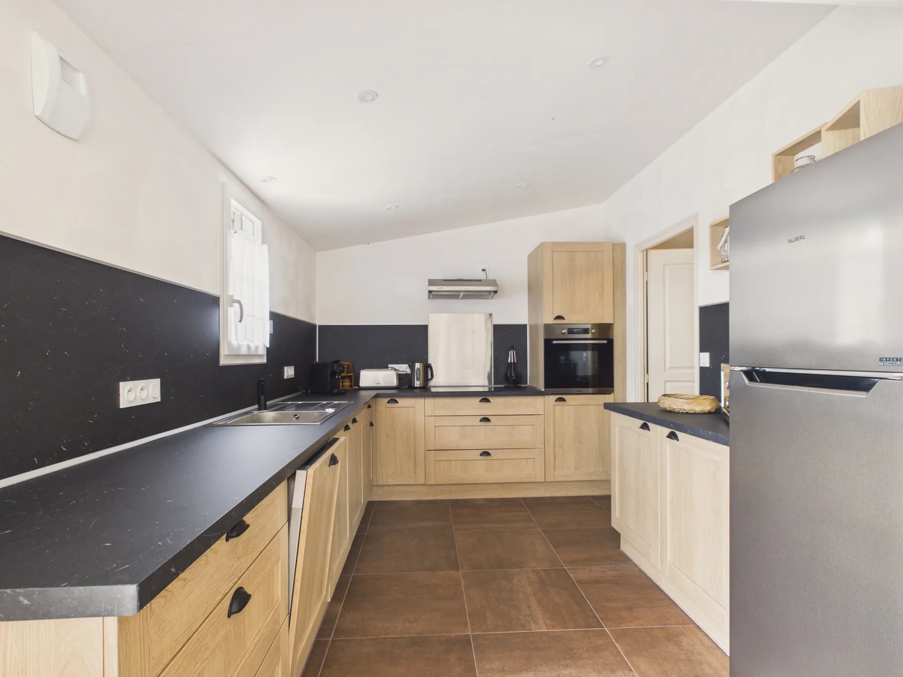 A bright kitchen with light wood cabinets and dark countertops.