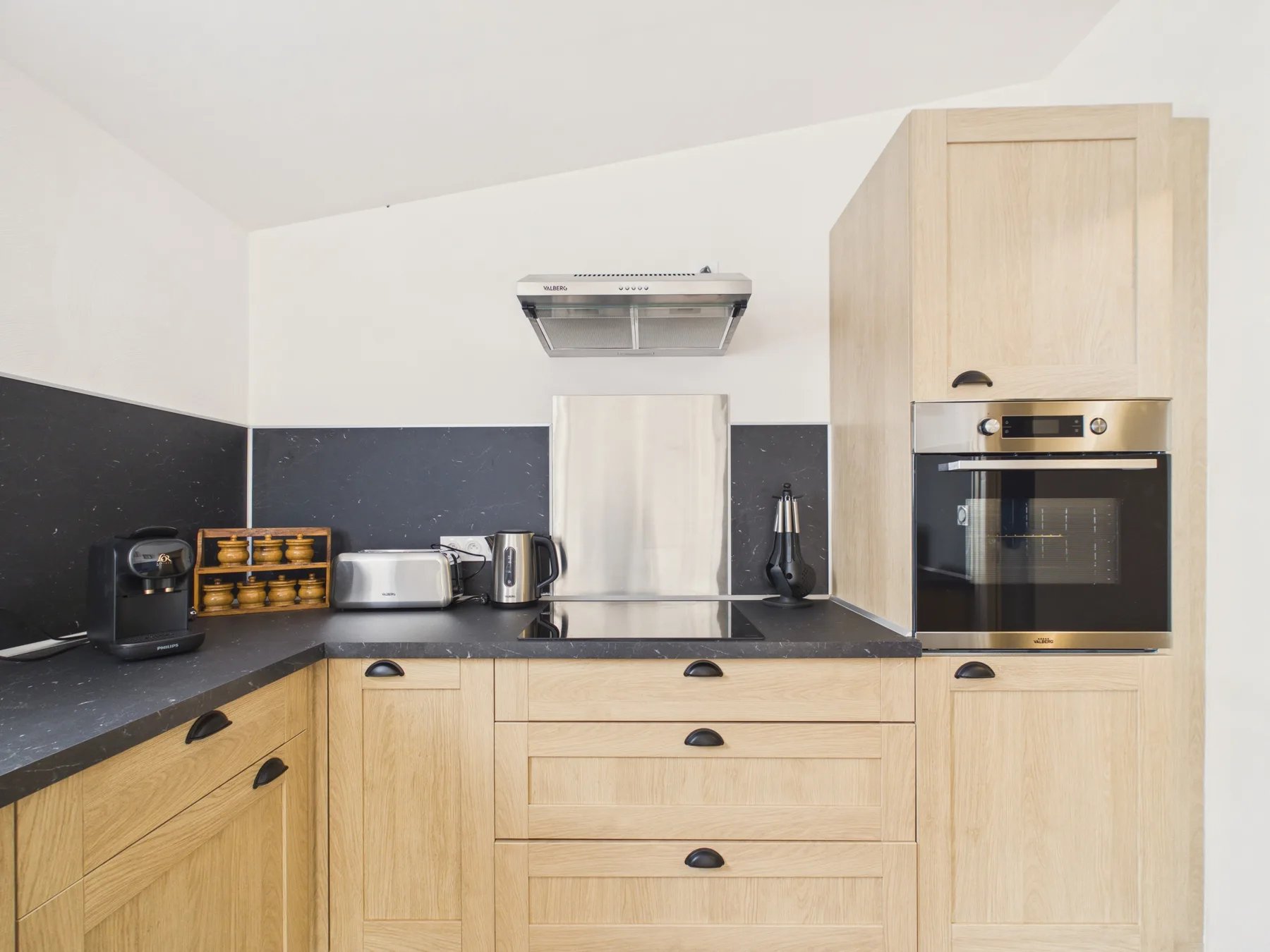 A modern kitchen with light wood cabinetry, dark countertops, and built-in appliances.