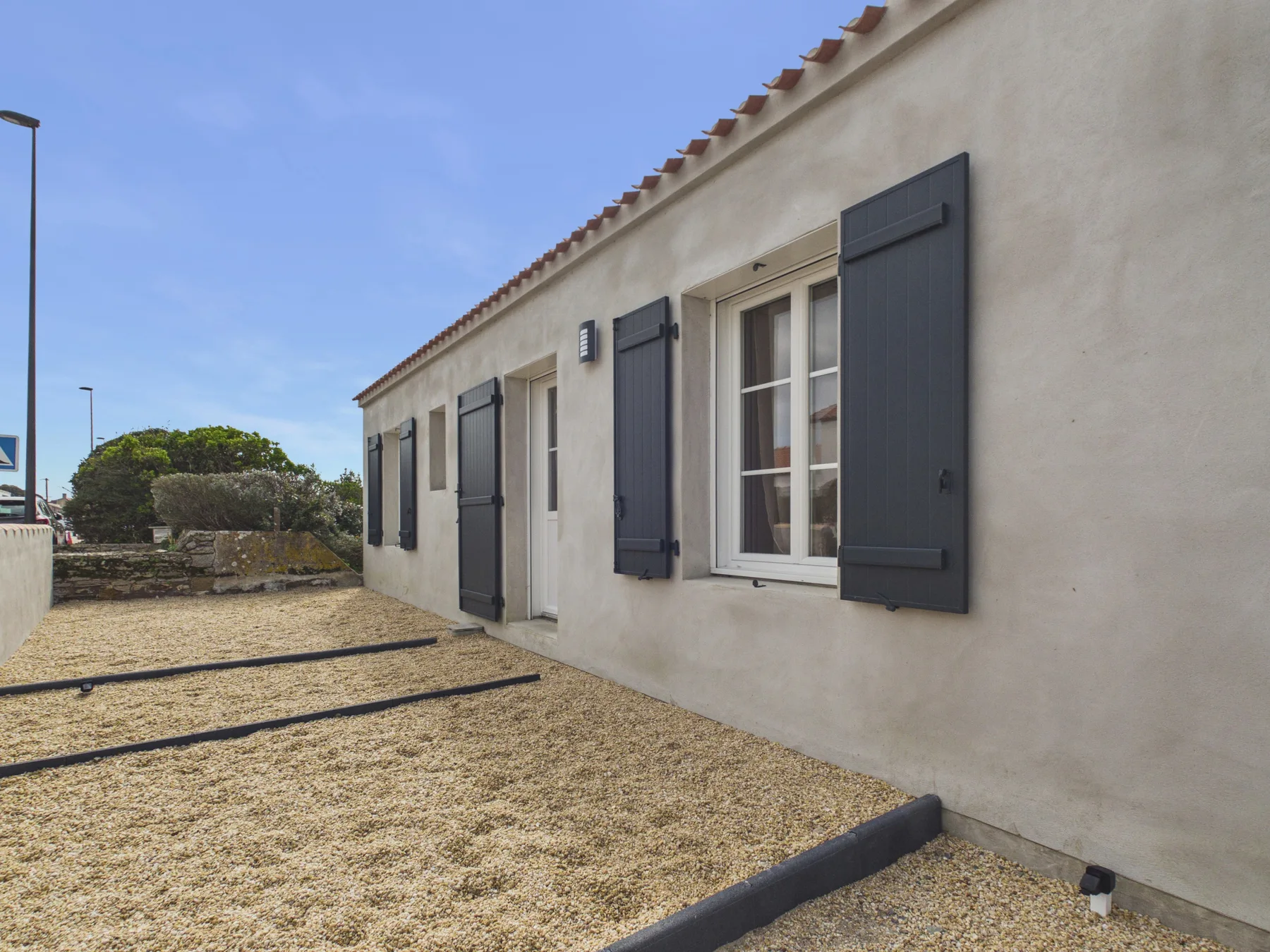 A light-colored building with dark shutters borders a gravel courtyard.