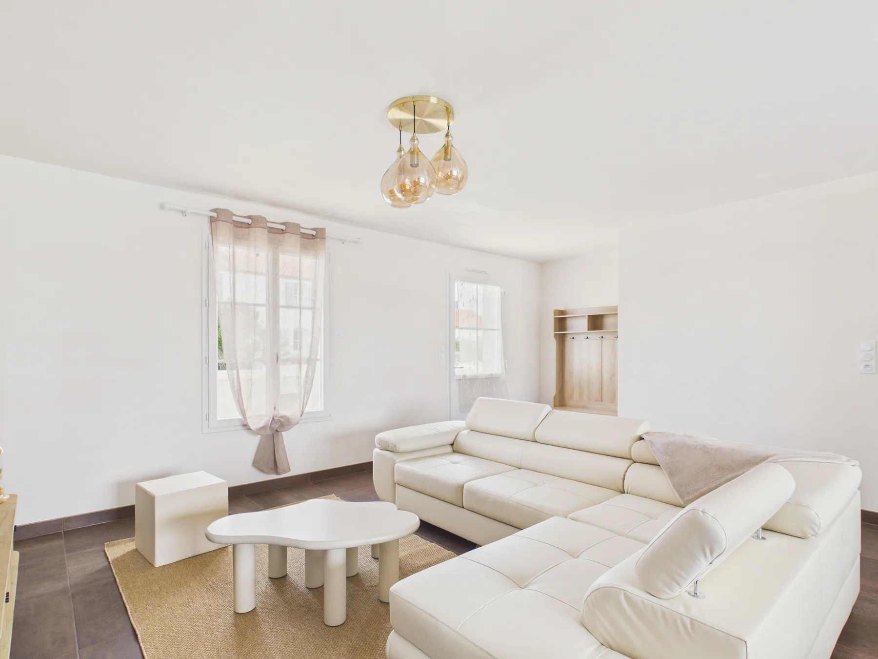 Bright living room with white seating, a low table, and a curtained window.