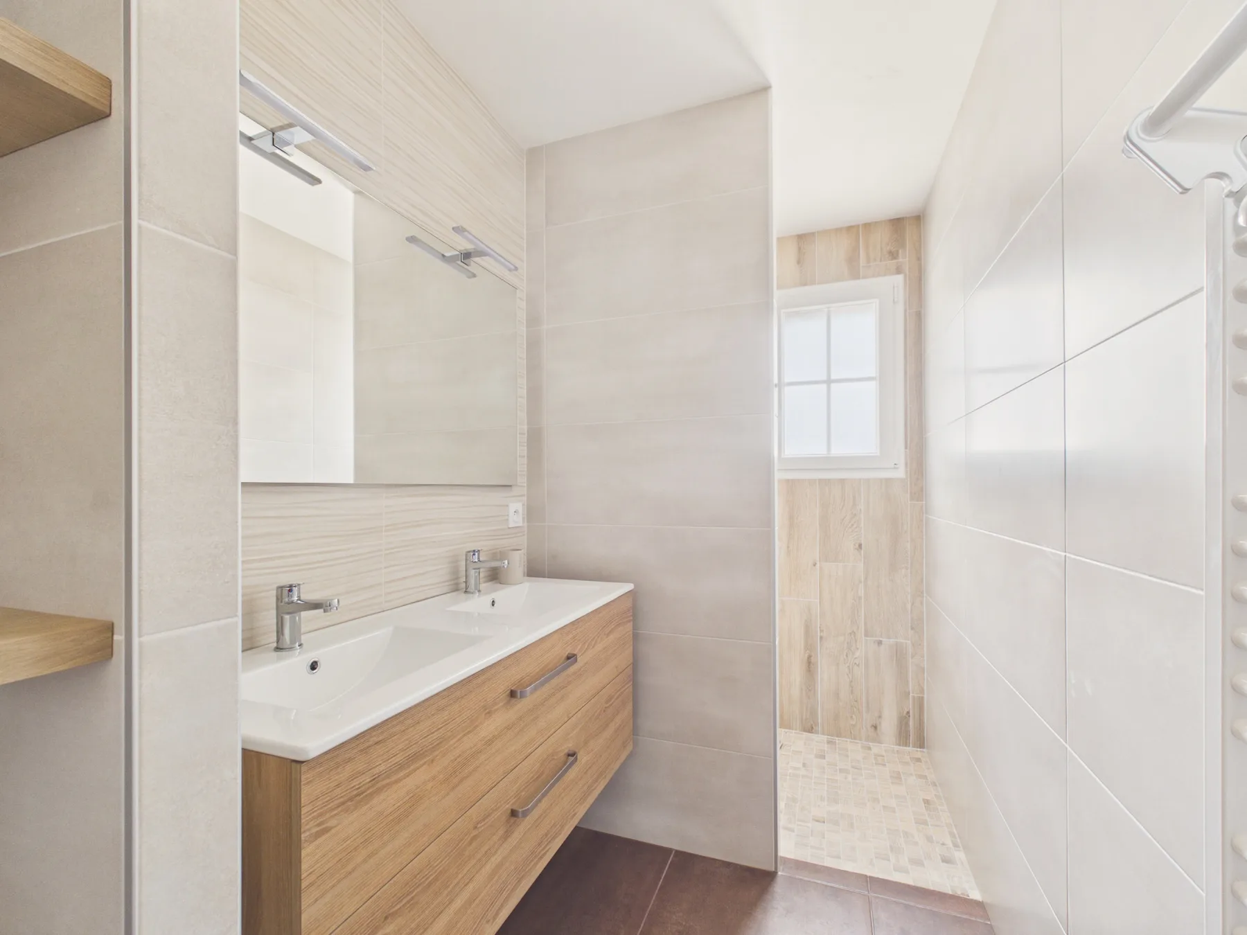 A bright bathroom with a wood vanity, sink, and walk-in shower.