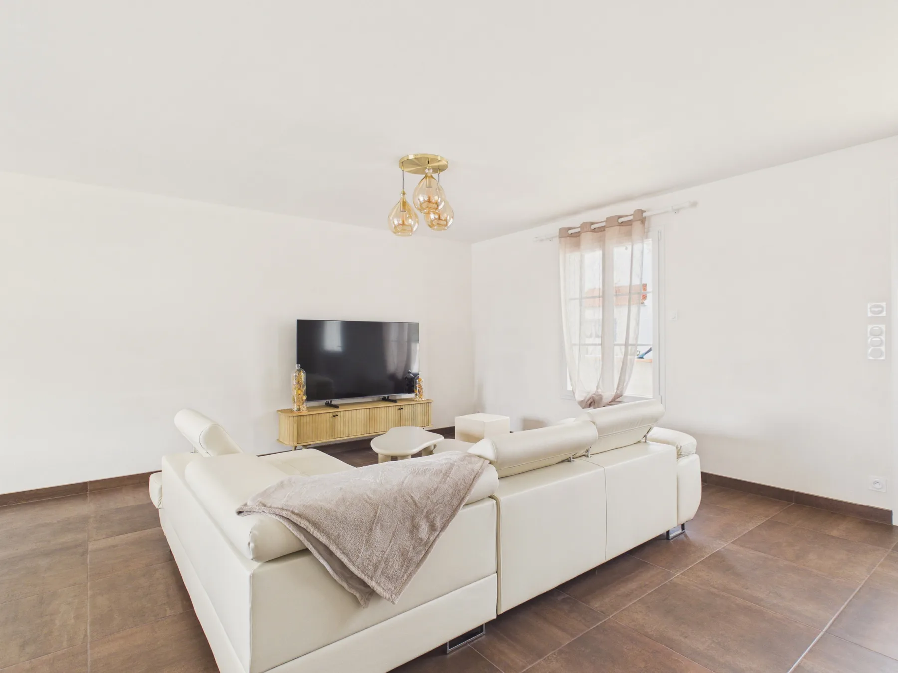 A bright living room with white seating and a television.