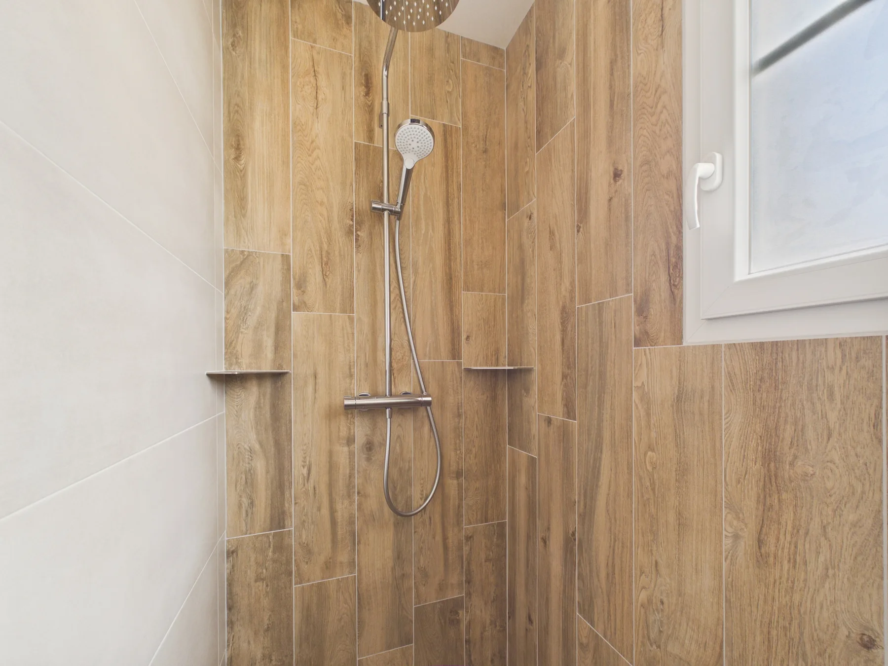 A tiled shower area has a wall-mounted showerhead and handheld sprayer.