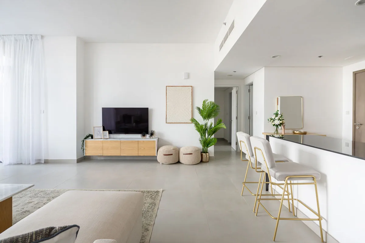 Una luminosa sala de estar y comedor con televisor, asientos y una barra larga.