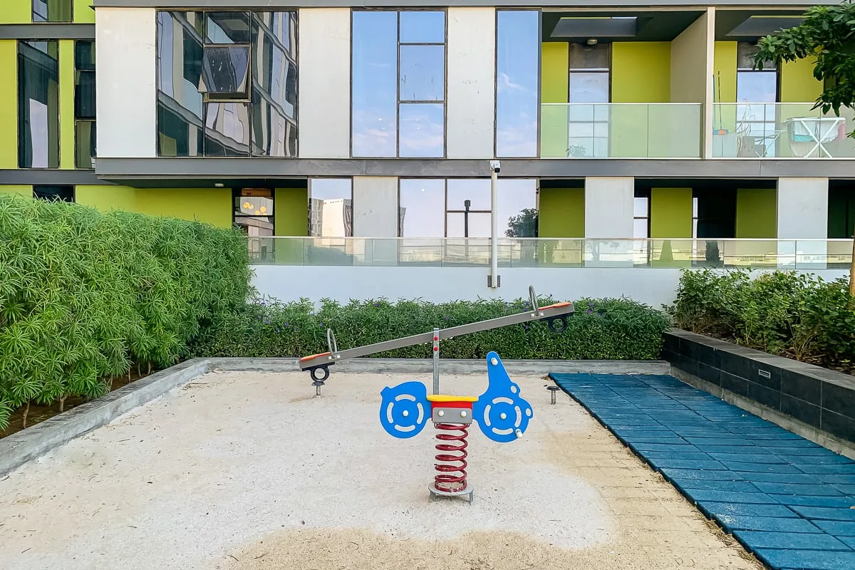 Un pequeño parque infantil con un balancín de resorte está junto a un camino azul pavimentado.