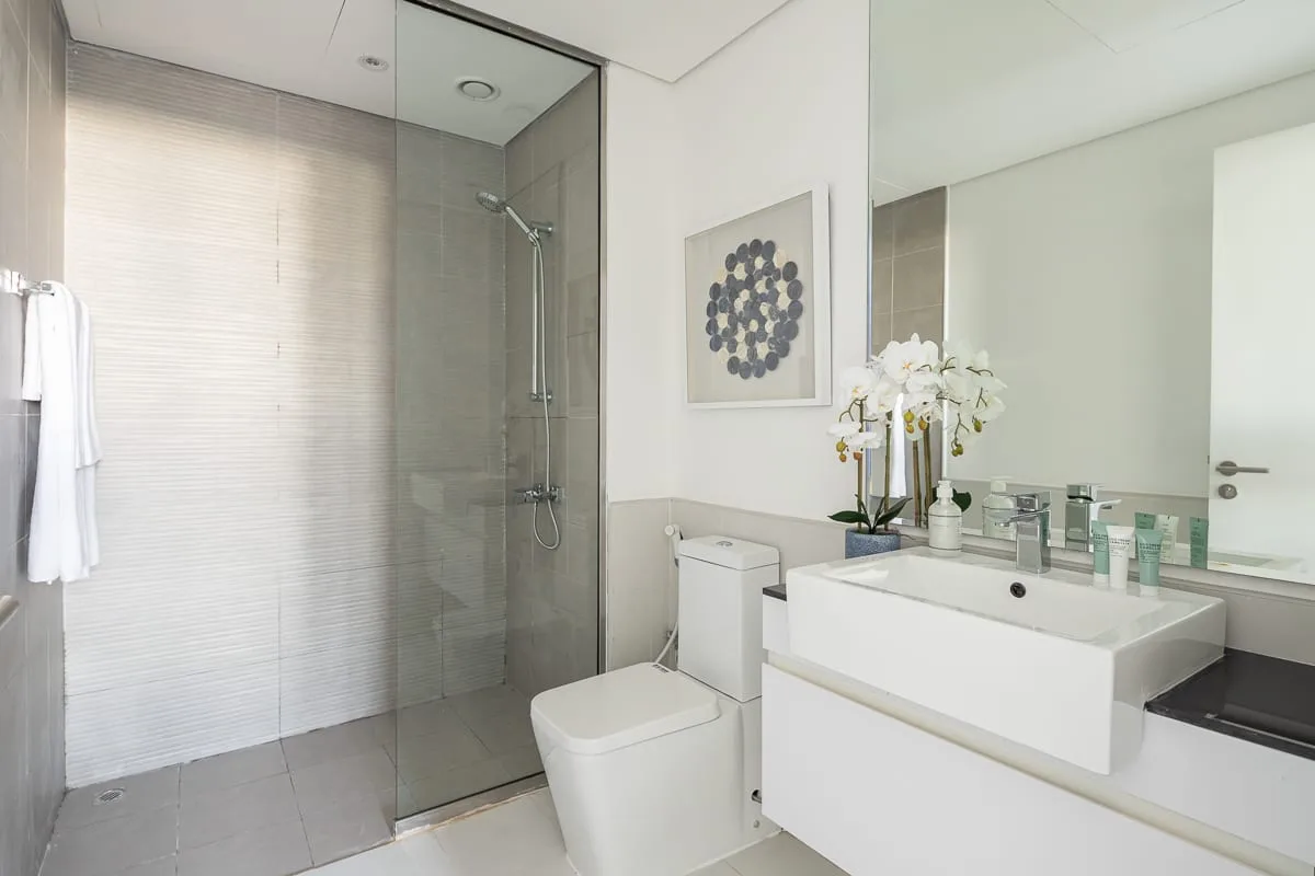 Un baño luminoso con ducha de vidrio, inodoro y tocador blanco.
