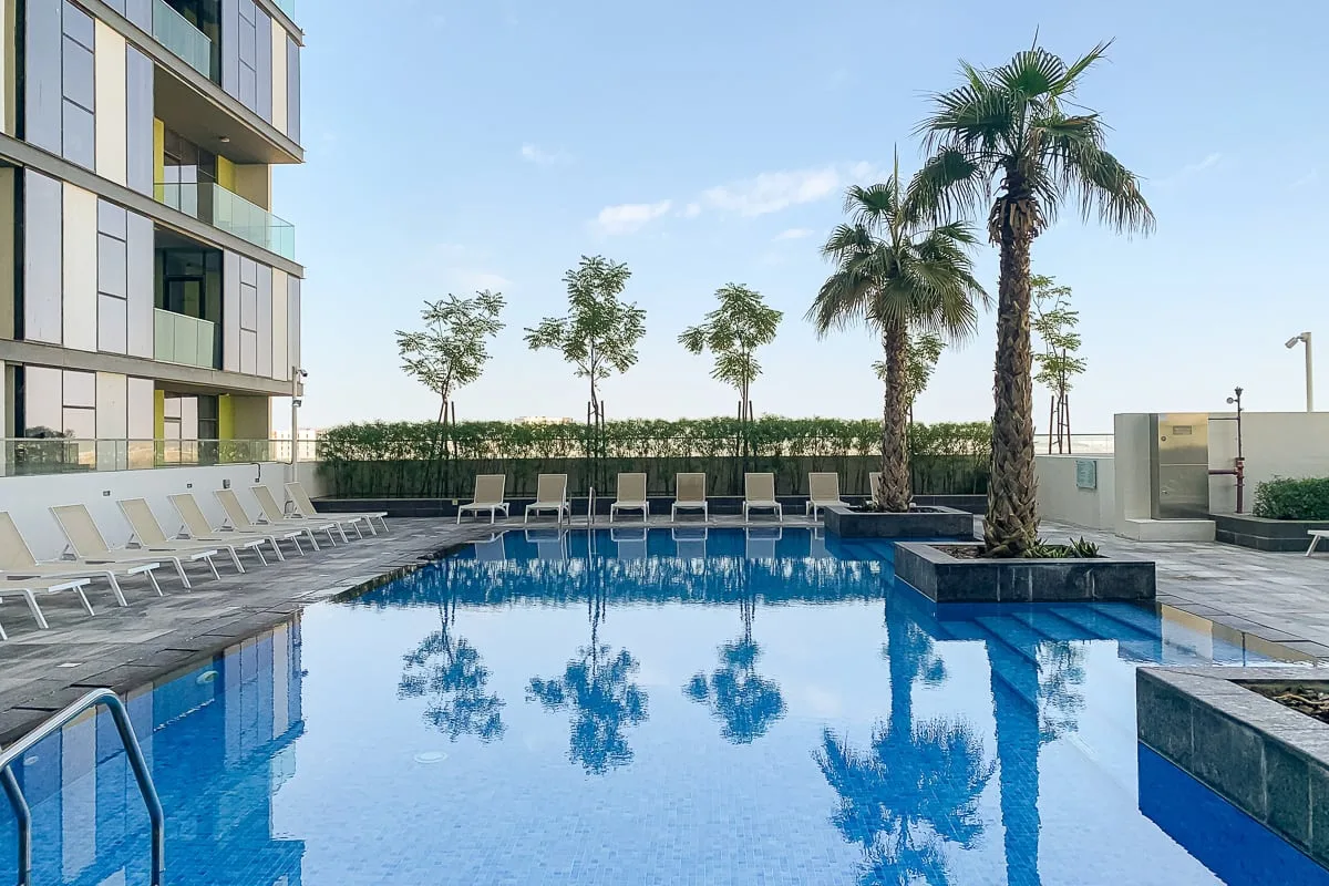 Una piscina al aire libre junto a un edificio moderno, con palmeras y tumbonas.