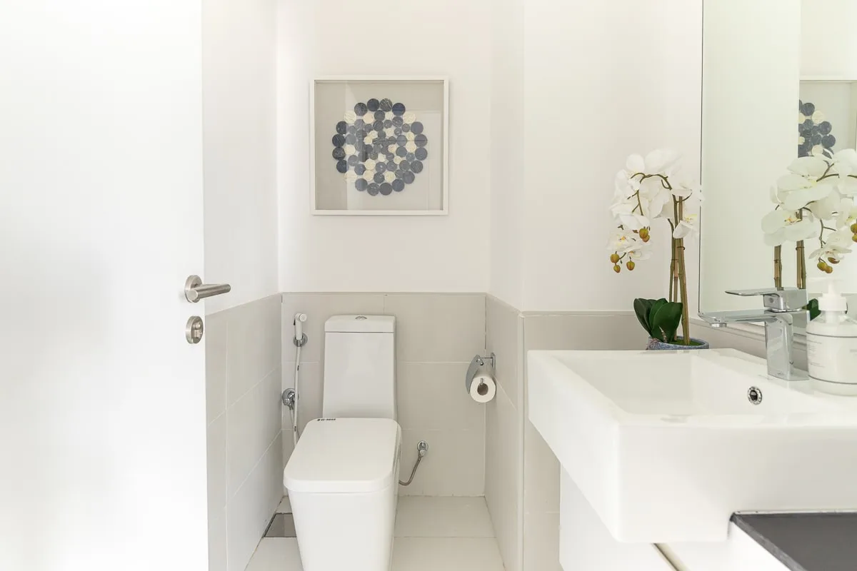 Un baño luminoso con un inodoro, arte en la pared y un lavabo blanco.