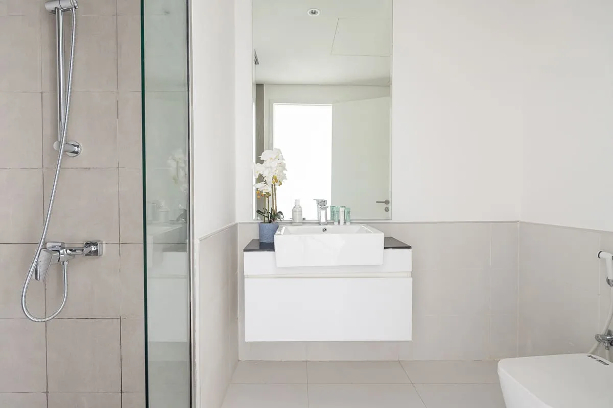 Un baño luminoso con ducha de vidrio, lavabo y un espejo grande.