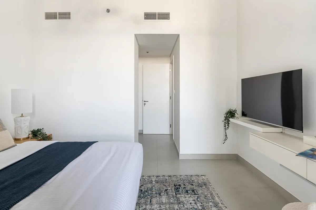 Un dormitorio luminoso con una cama, un televisor y una puerta.