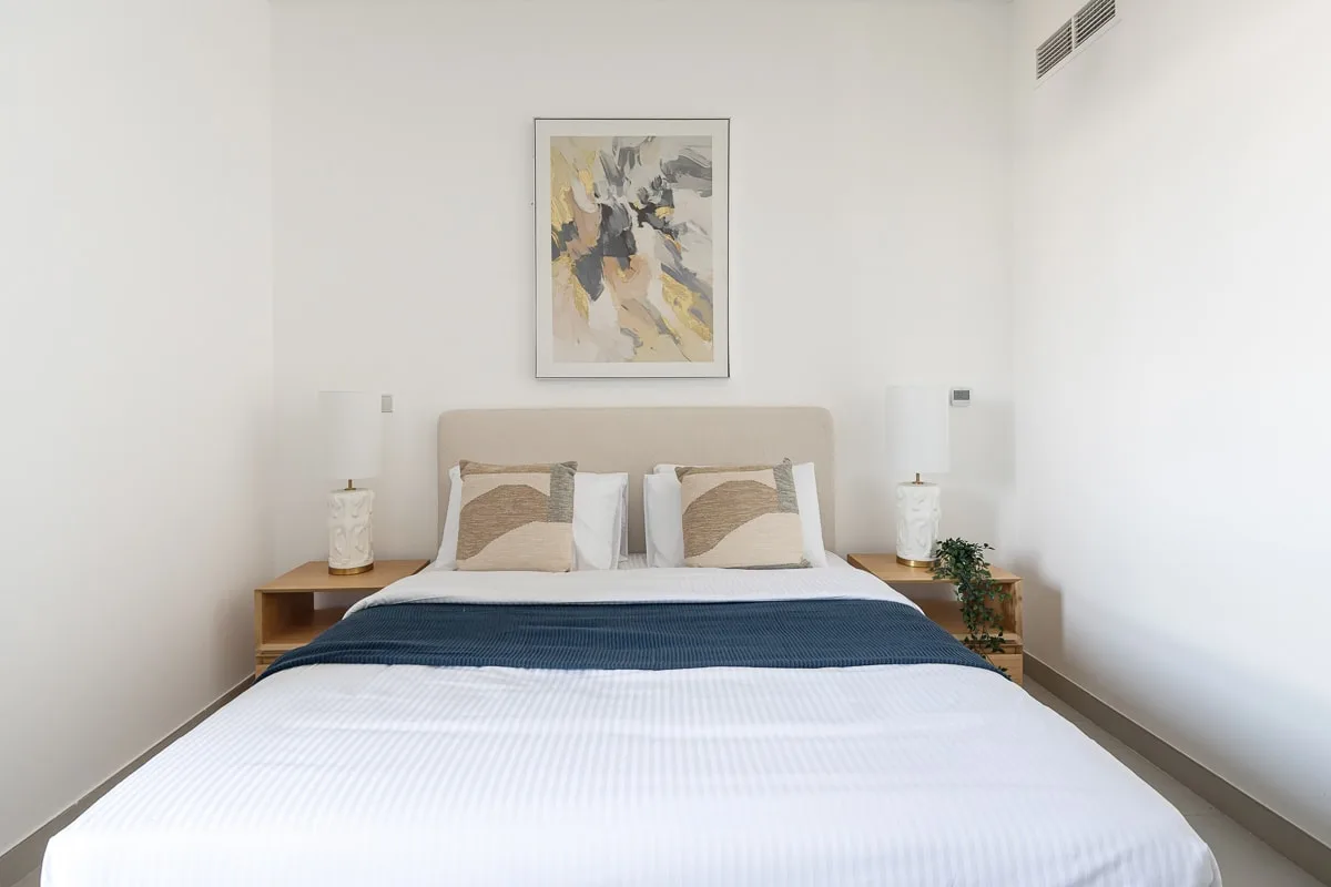 Un dormitorio luminoso con una cama bien tendida y una obra abstracta sobre el cabecero.