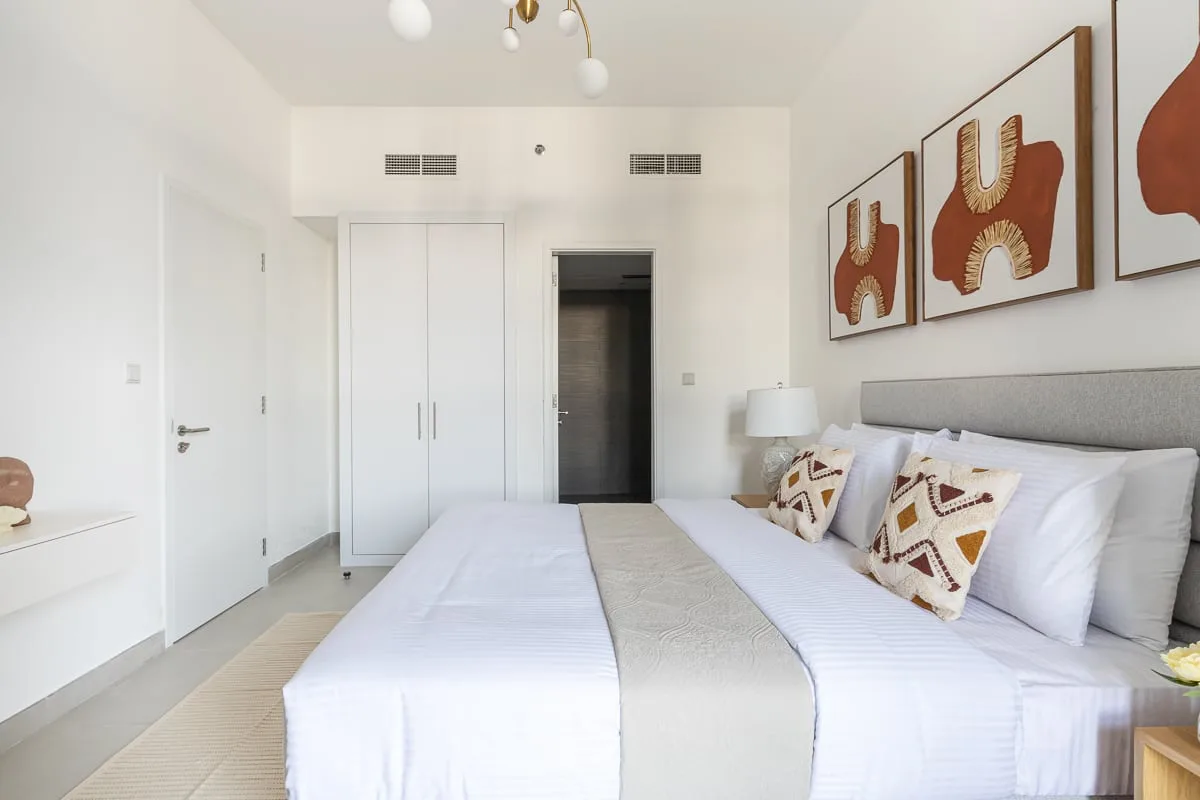 Un dormitorio luminoso con una cama bien tendida y cuadros enmarcados sobre el cabecero.