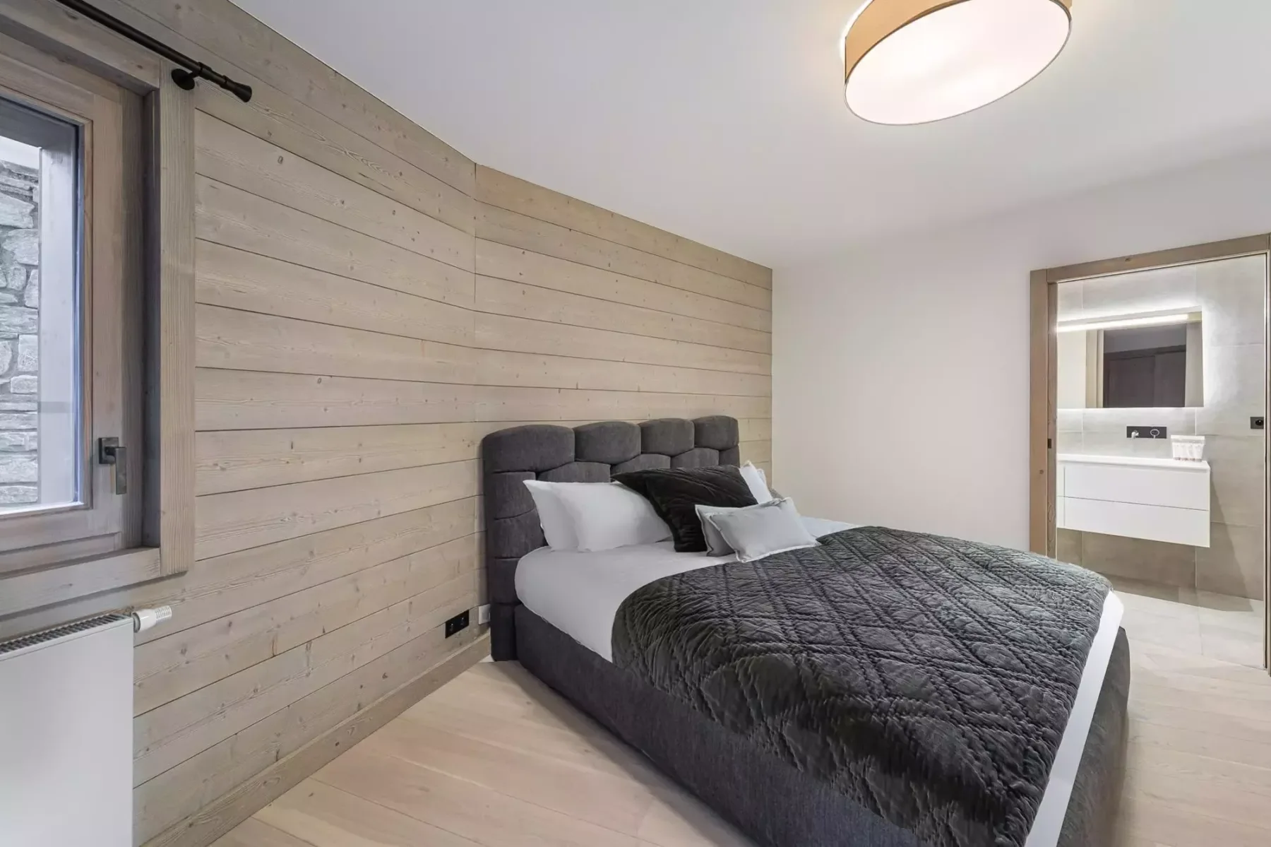 Un dormitorio con una cama junto a una pared revestida de madera clara y una puerta abierta al baño.