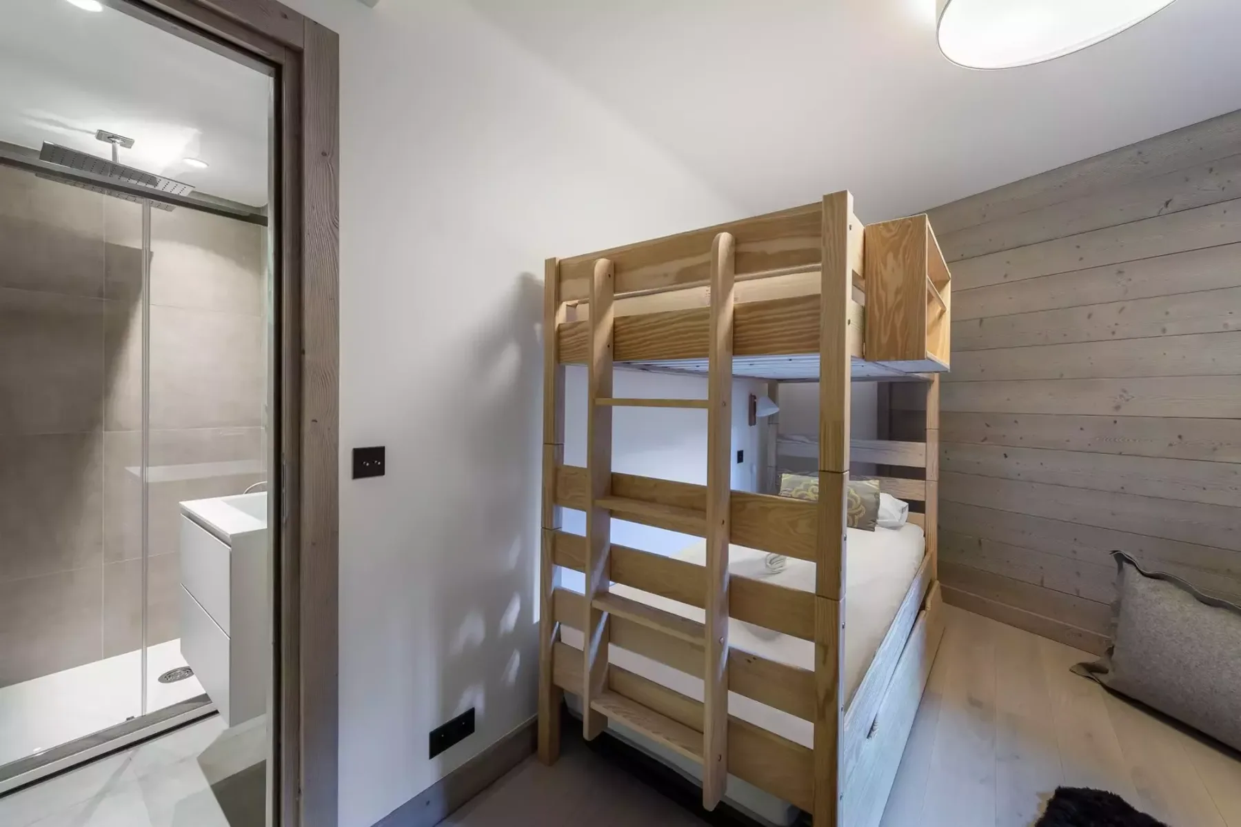 Un dormitorio con una litera de madera junto a una puerta abierta al baño.
