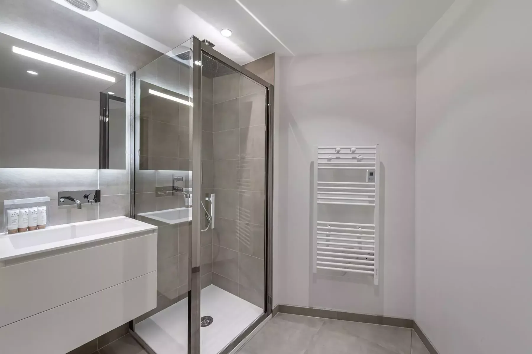 Un baño moderno con ducha de vidrio, lavabo y toallero calefactable de pared.