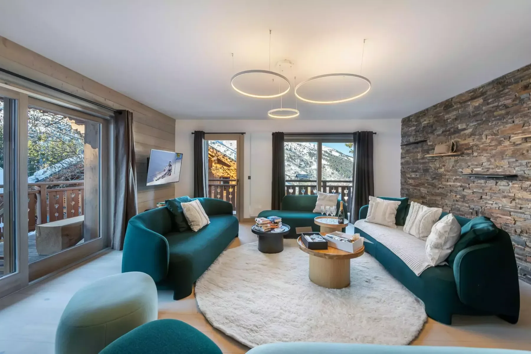 A bright living room with teal seating, a light rug, and large windows.