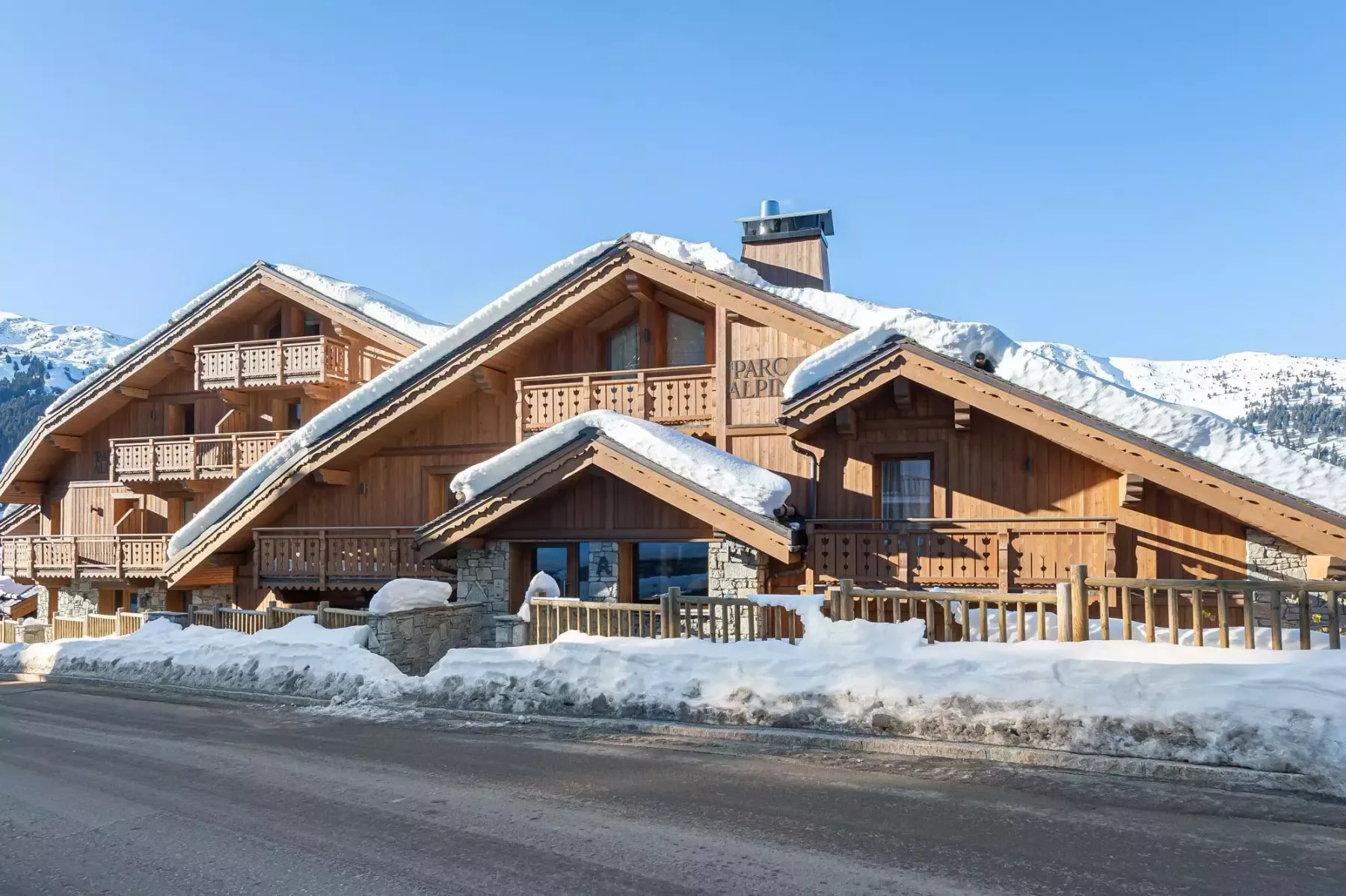 Edificios de chalés de madera cubiertos de nieve junto a una carretera, con montañas al fondo.