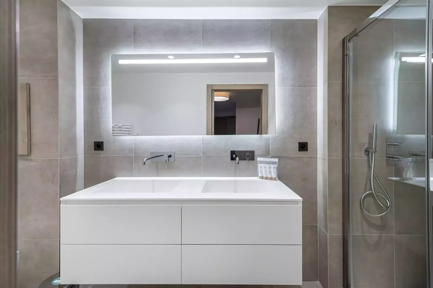 Un baño moderno con un amplio lavabo, espejo iluminado y ducha de vidrio.