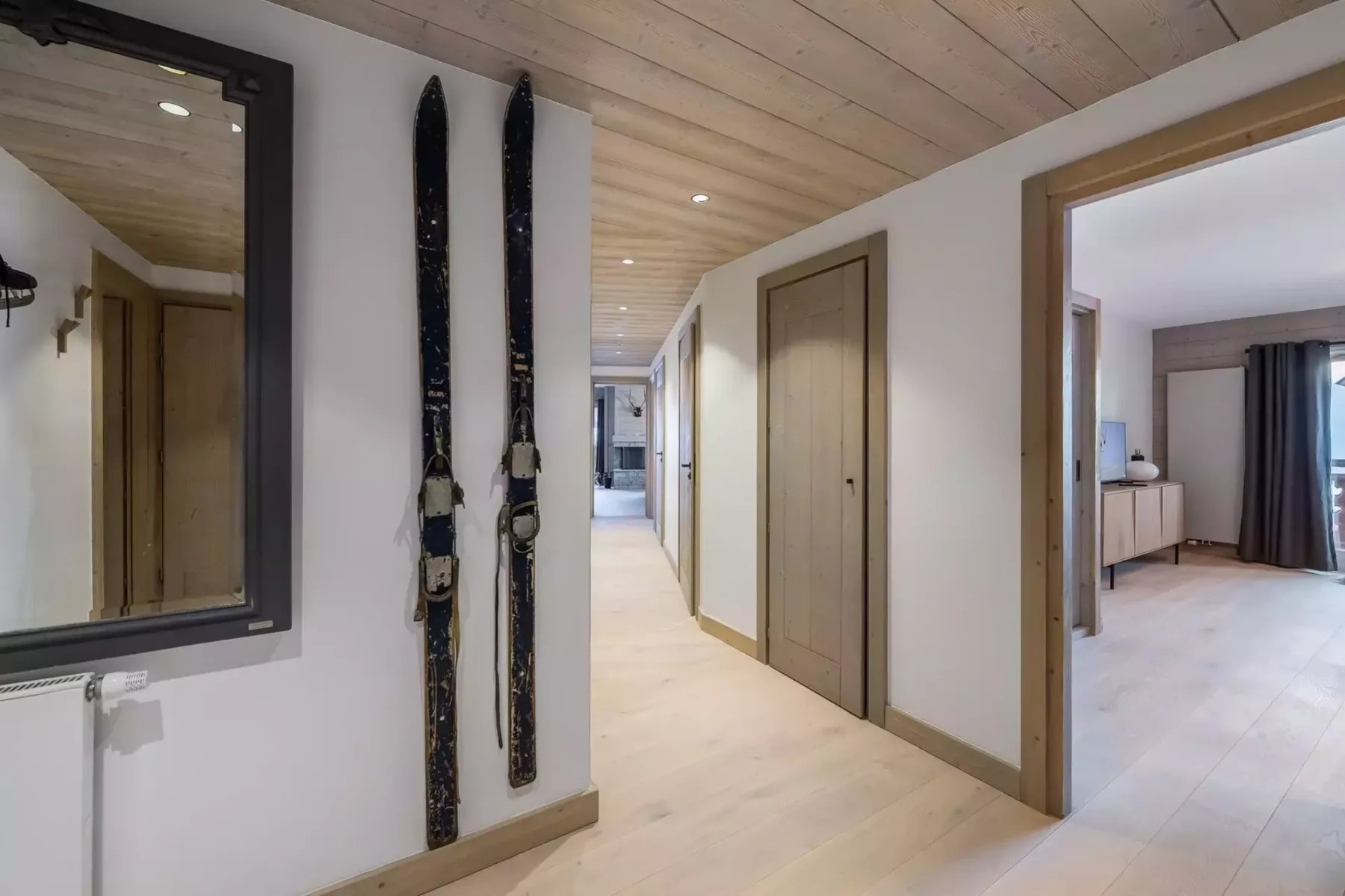 Un pasillo luminoso con suelo de madera clara y esquís junto a un espejo.