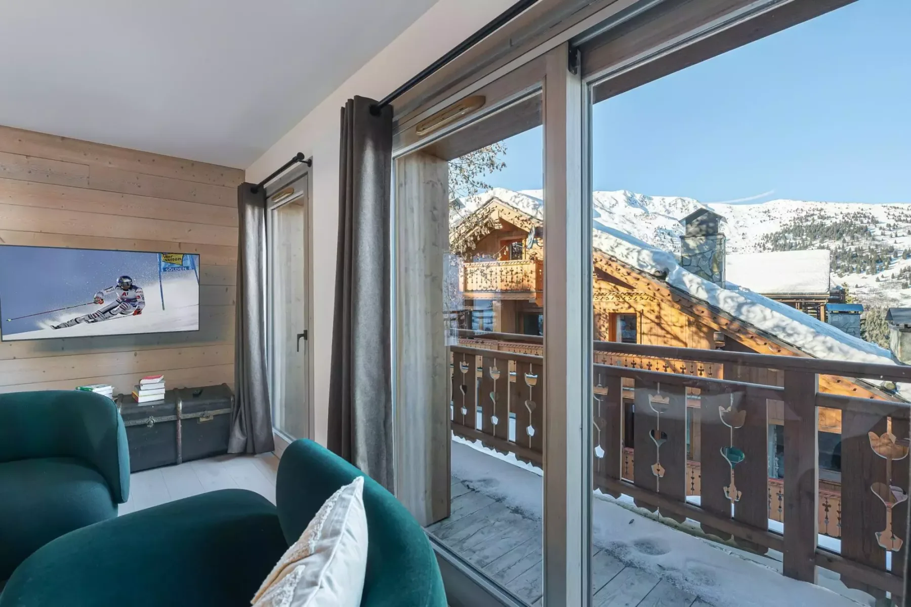 A living room with teal seating and large windows overlooking snowy mountain buildings.