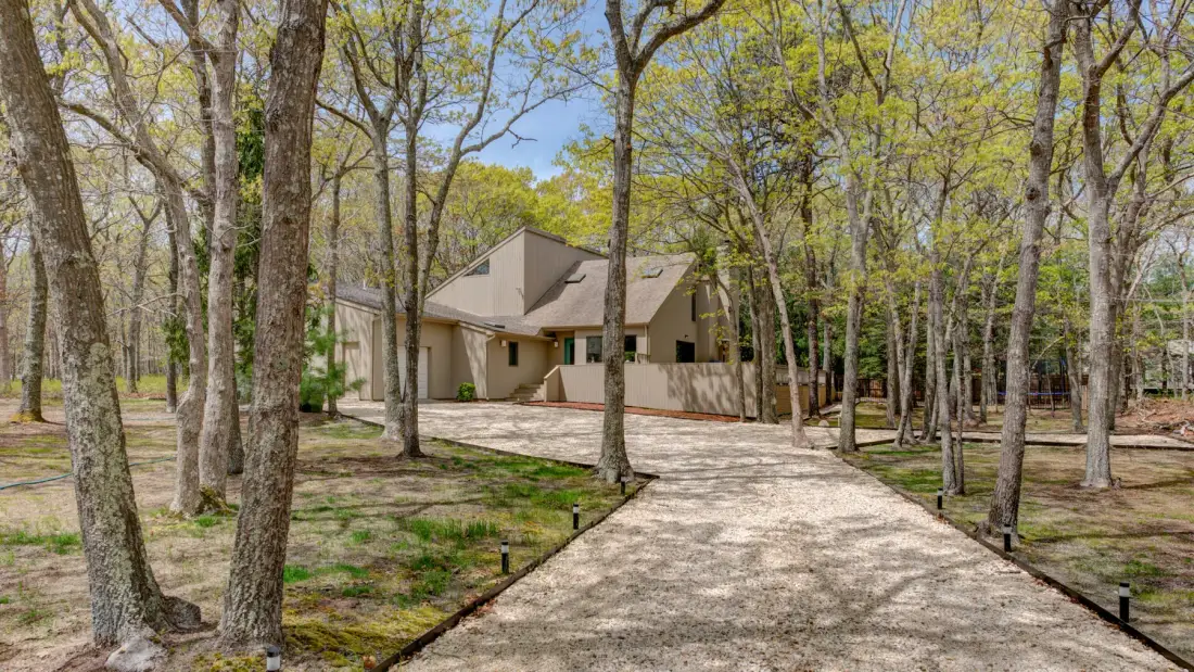 A house stands at the end of a paved driveway among trees.