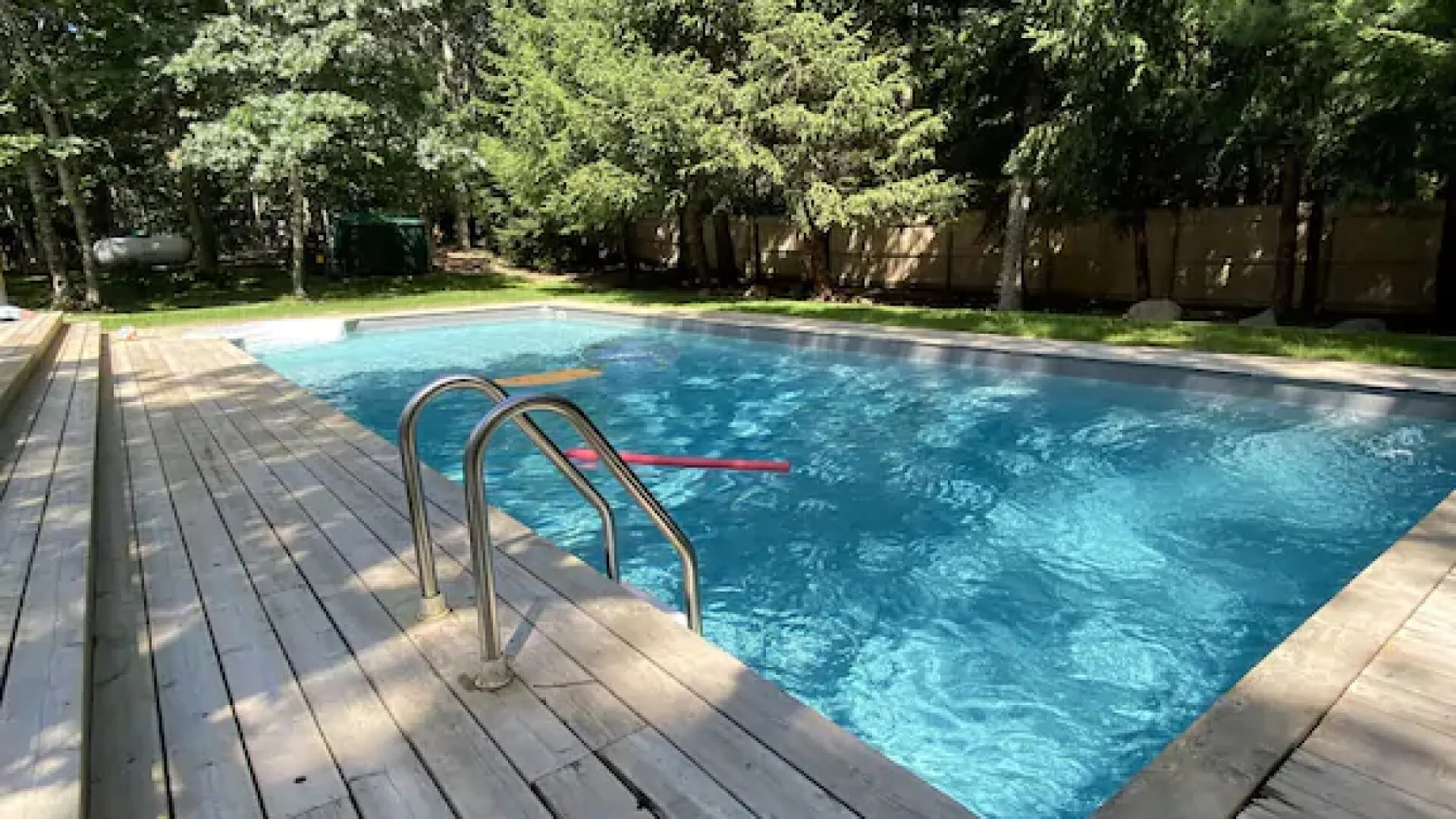 Una piscina al aire libre está rodeada por una terraza de madera y árboles frondosos.