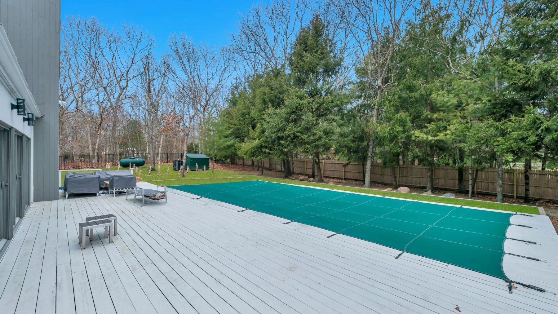 Una amplia terraza exterior junto a una piscina cubierta y un patio arbolado.