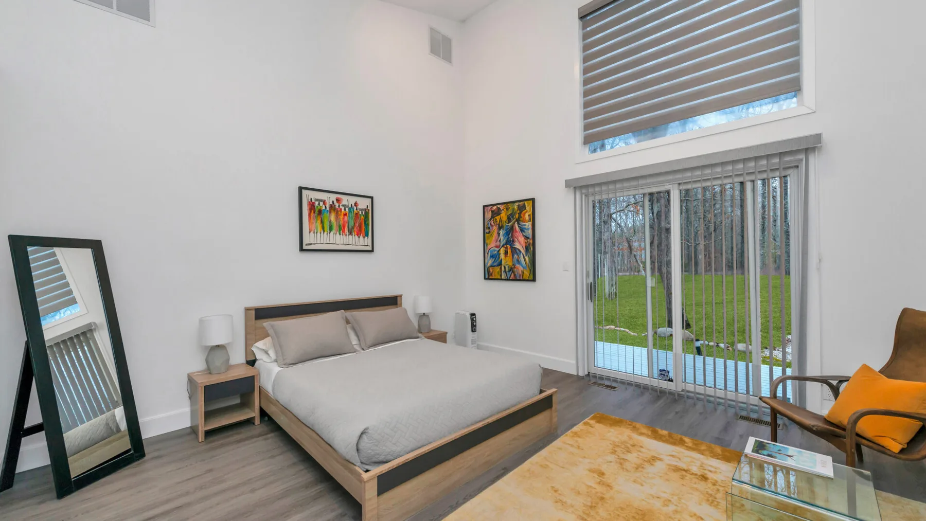 Un dormitorio con una cama, mesitas de noche y una ventana grande con vista al jardín.